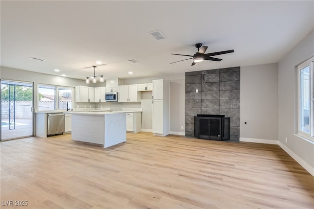 kitchen with a fireplace, decorative light fixtures, a kitchen island, white cabinetry, and stainless steel appliances