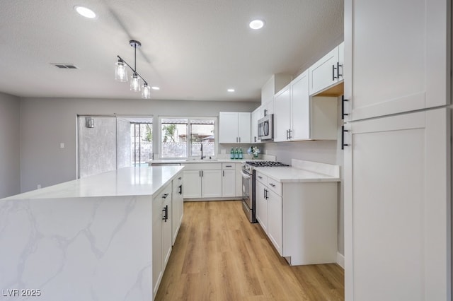 kitchen with pendant lighting, white cabinets, light hardwood / wood-style flooring, a kitchen island, and stainless steel appliances