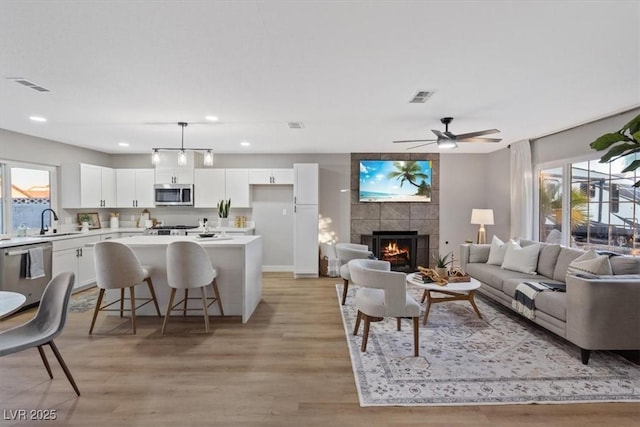 living room with light hardwood / wood-style flooring, a tiled fireplace, ceiling fan, and sink