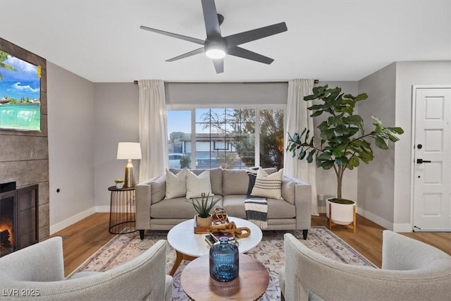 living room featuring hardwood / wood-style floors, ceiling fan, and a tiled fireplace