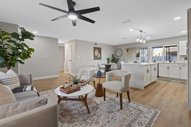 living room featuring sink, light hardwood / wood-style floors, and ceiling fan with notable chandelier