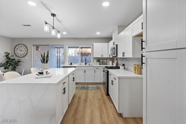 kitchen featuring white cabinets, appliances with stainless steel finishes, and decorative light fixtures