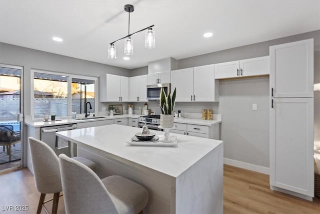 kitchen featuring white cabinetry, a center island, sink, hanging light fixtures, and stainless steel appliances