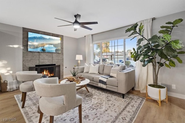 living room featuring ceiling fan, light hardwood / wood-style floors, and a tiled fireplace