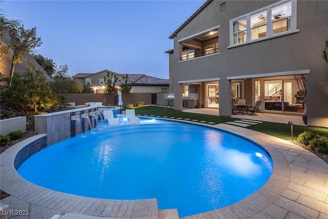 pool at dusk with pool water feature, a bar, and a patio