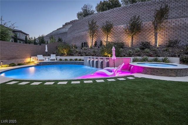 pool at dusk with an in ground hot tub and a yard