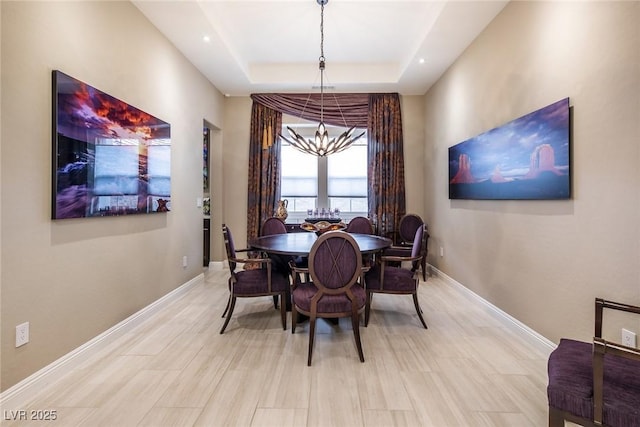 dining room with a raised ceiling, a chandelier, and light wood-type flooring