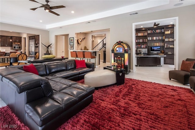 living room featuring built in shelves, ceiling fan, and a raised ceiling