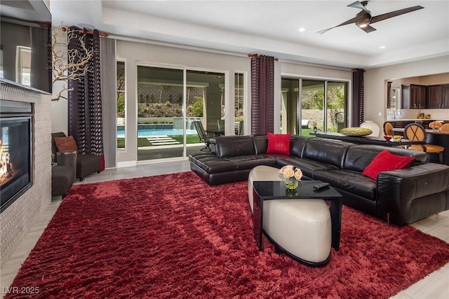 living room featuring a raised ceiling, ceiling fan, light hardwood / wood-style floors, and a brick fireplace