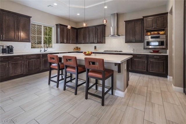 kitchen featuring appliances with stainless steel finishes, wall chimney exhaust hood, sink, a center island, and a breakfast bar area