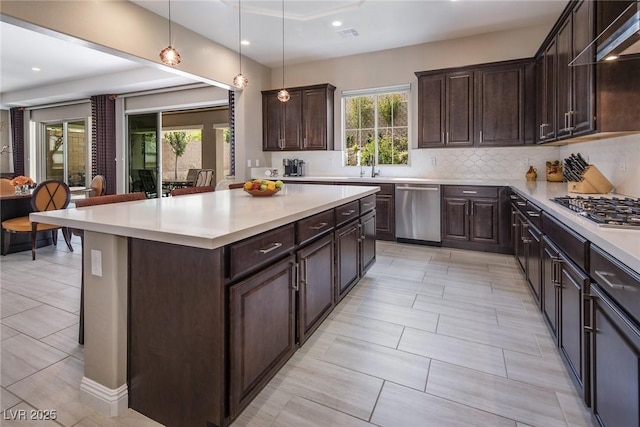 kitchen featuring wall chimney exhaust hood, stainless steel appliances, plenty of natural light, pendant lighting, and a kitchen island