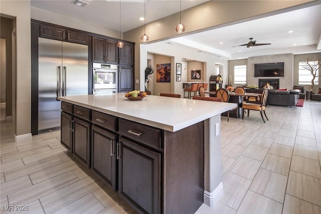 kitchen with decorative light fixtures, dark brown cabinetry, a fireplace, and appliances with stainless steel finishes