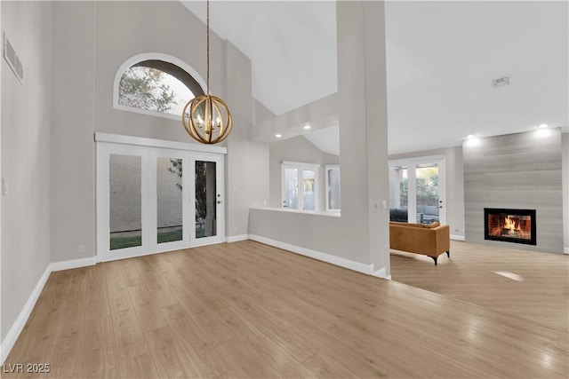 unfurnished living room featuring a notable chandelier, a large fireplace, light wood-type flooring, and high vaulted ceiling