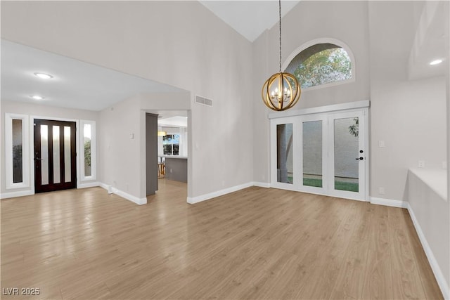 entrance foyer with a healthy amount of sunlight, light wood-type flooring, high vaulted ceiling, and a notable chandelier