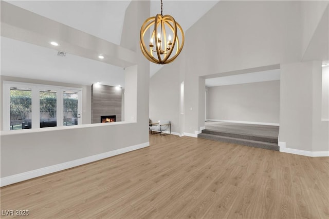 unfurnished living room featuring a fireplace, wood-type flooring, an inviting chandelier, and high vaulted ceiling