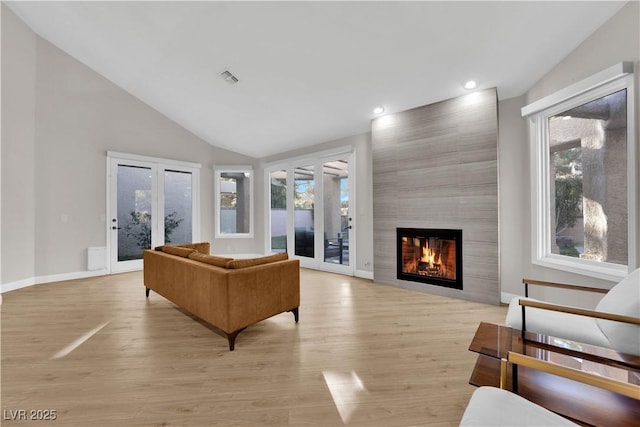 living room featuring french doors, light wood-type flooring, plenty of natural light, and a tiled fireplace