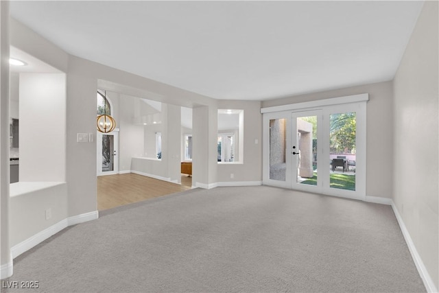 carpeted empty room with french doors and an inviting chandelier