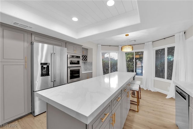 kitchen with appliances with stainless steel finishes, gray cabinetry, light hardwood / wood-style floors, a kitchen island, and hanging light fixtures