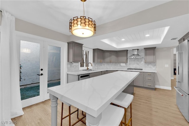 kitchen featuring gray cabinetry, wall chimney exhaust hood, hanging light fixtures, a raised ceiling, and a kitchen island