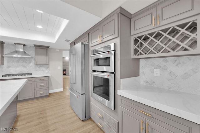 kitchen featuring decorative backsplash, wall chimney exhaust hood, light hardwood / wood-style floors, stainless steel appliances, and gray cabinets