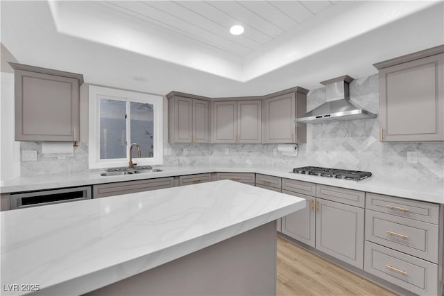 kitchen featuring gray cabinetry, sink, wall chimney exhaust hood, stainless steel gas stovetop, and a tray ceiling