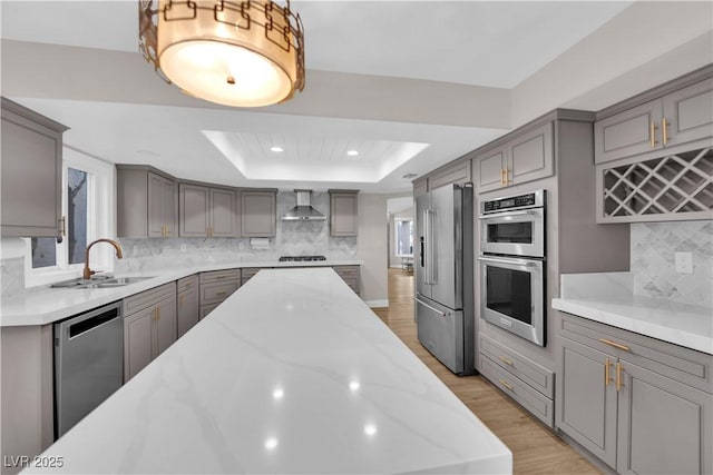 kitchen featuring sink, wall chimney exhaust hood, a tray ceiling, decorative backsplash, and appliances with stainless steel finishes