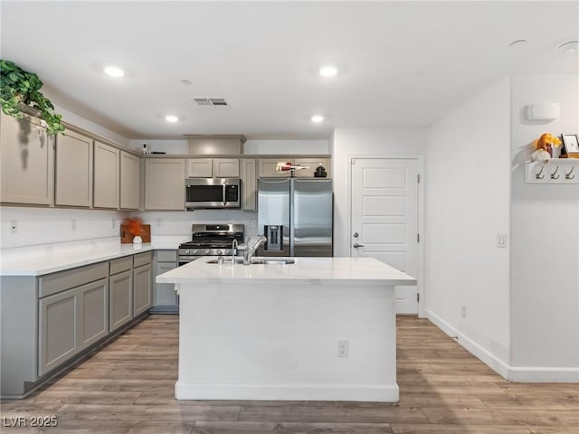 kitchen with stainless steel appliances, light hardwood / wood-style flooring, a center island with sink, and gray cabinetry