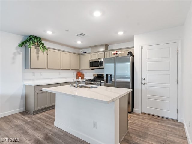 kitchen with sink, stainless steel appliances, an island with sink, gray cabinets, and light wood-type flooring