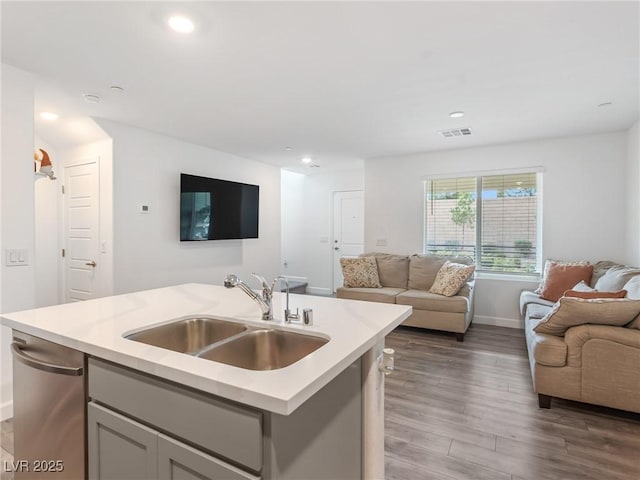 kitchen with sink, light hardwood / wood-style floors, gray cabinetry, and an island with sink