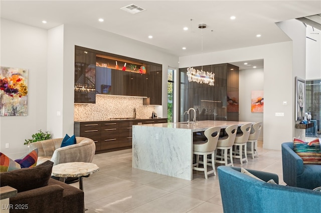 kitchen with dark brown cabinetry, sink, a kitchen breakfast bar, decorative light fixtures, and decorative backsplash