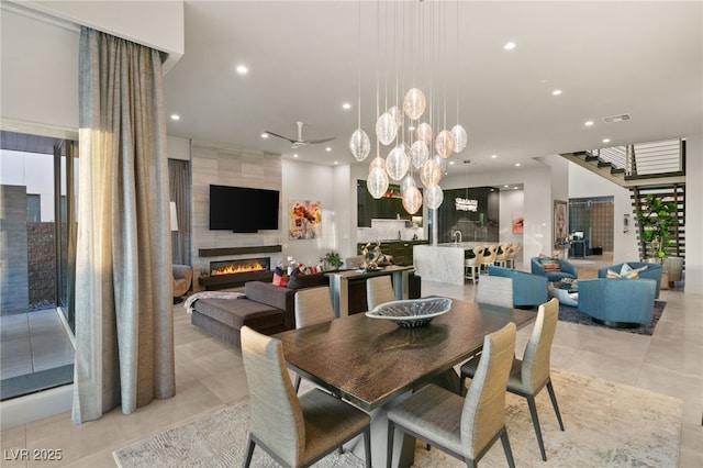 dining area with ceiling fan with notable chandelier and a tile fireplace