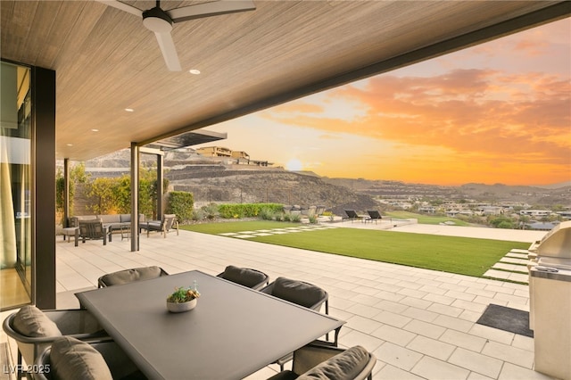 patio terrace at dusk featuring ceiling fan, a yard, a mountain view, and an outdoor hangout area