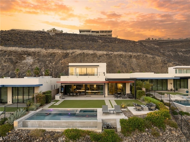 back house at dusk with an outdoor living space, a swimming pool with hot tub, a balcony, and a patio