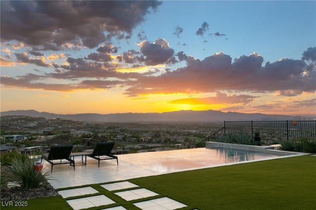 pool at dusk with a patio area, a mountain view, and a yard