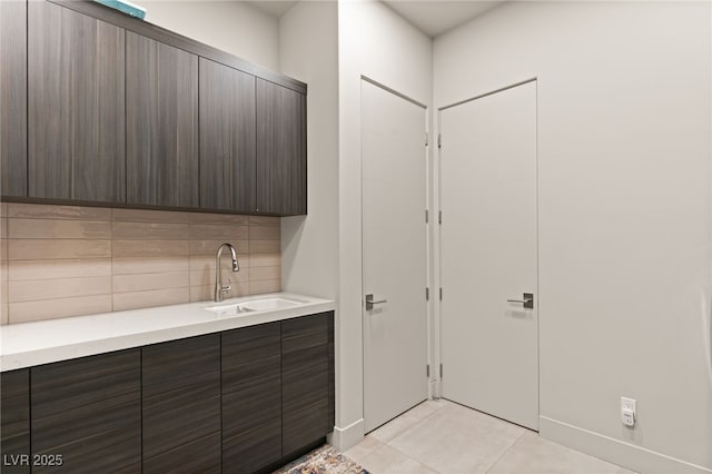 interior space with decorative backsplash, light tile patterned floors, dark brown cabinetry, and sink