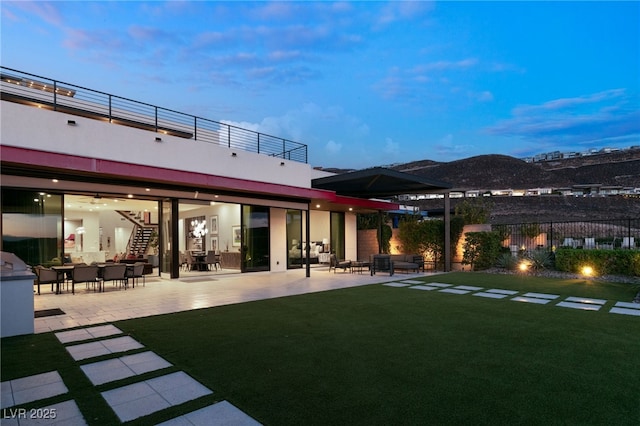 back house at dusk featuring a yard and a patio