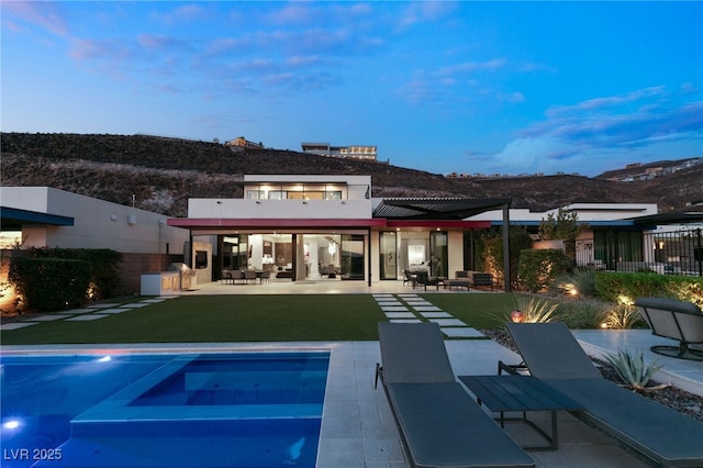 back house at dusk featuring a mountain view, a patio area, and a yard