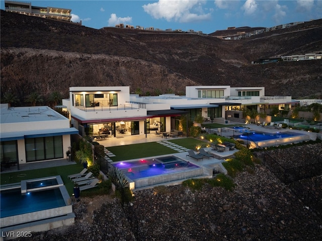 rear view of property with an in ground hot tub, a mountain view, a balcony, and a patio