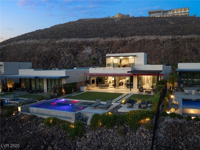 back house at dusk featuring a mountain view, a patio, an in ground hot tub, and an outdoor living space