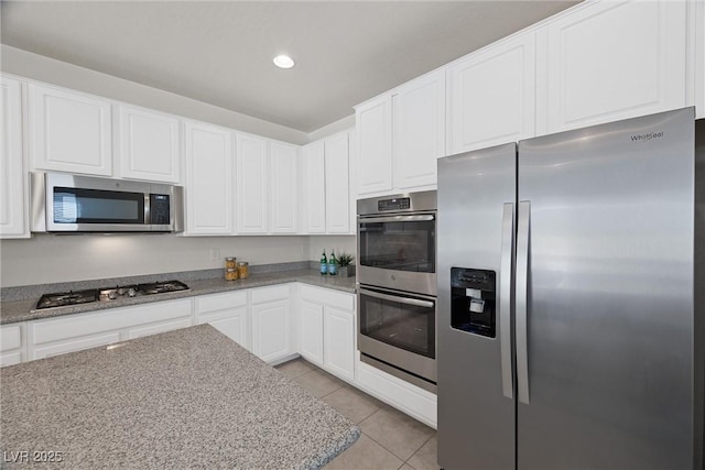 kitchen featuring light stone countertops, light tile patterned floors, stainless steel appliances, and white cabinetry