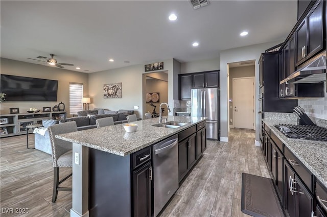 kitchen featuring stainless steel appliances, extractor fan, sink, light hardwood / wood-style floors, and an island with sink