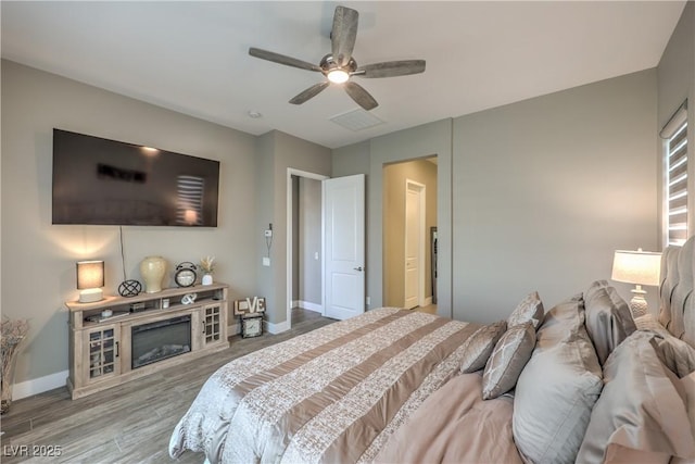 bedroom with a fireplace, light wood-type flooring, and ceiling fan