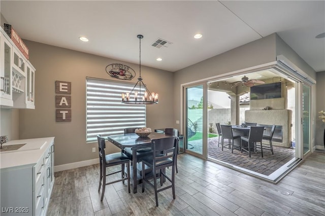 dining room with ceiling fan with notable chandelier, dark hardwood / wood-style flooring, and a fireplace