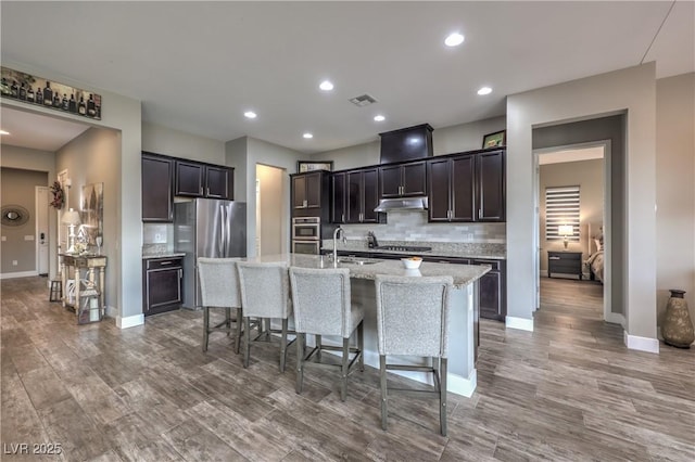 kitchen featuring decorative backsplash, appliances with stainless steel finishes, sink, a center island with sink, and a breakfast bar area