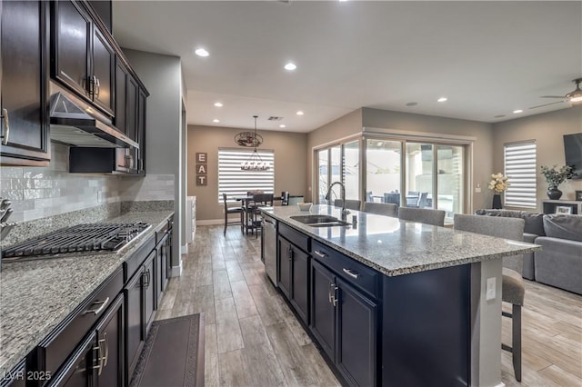 kitchen with a center island with sink, a kitchen breakfast bar, sink, appliances with stainless steel finishes, and light stone counters