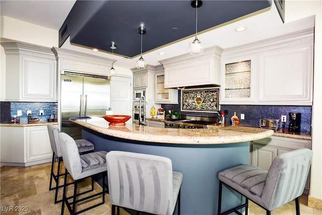 kitchen with white cabinetry, tasteful backsplash, light stone counters, built in appliances, and pendant lighting