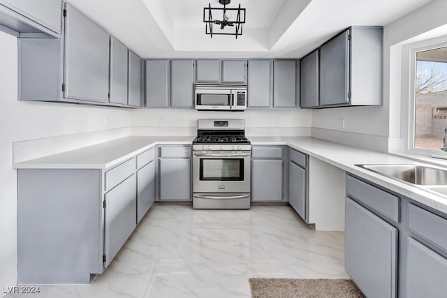 kitchen with sink, stainless steel appliances, an inviting chandelier, a tray ceiling, and gray cabinets