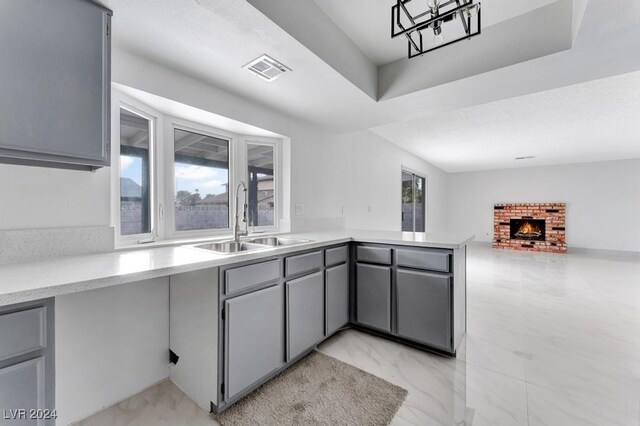 kitchen with a fireplace, gray cabinets, kitchen peninsula, and sink