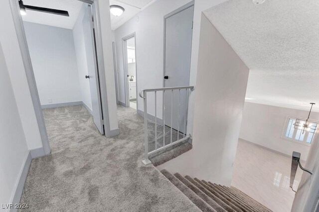 corridor with light carpet, a textured ceiling, and an inviting chandelier