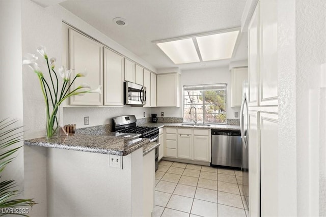 kitchen featuring sink, stone counters, white cabinetry, appliances with stainless steel finishes, and kitchen peninsula